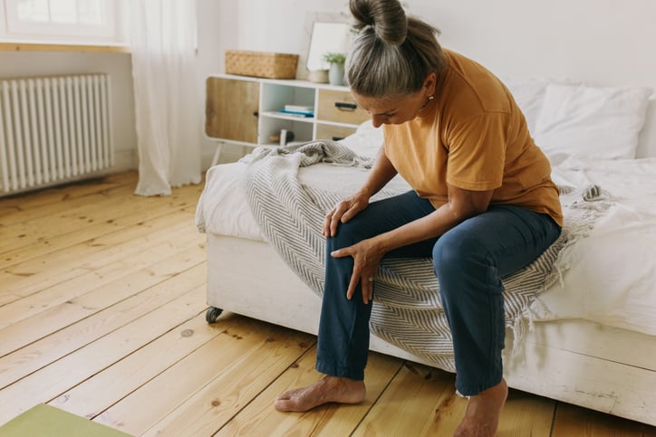 Vrouw zit op bed en voelt aan onderbeen