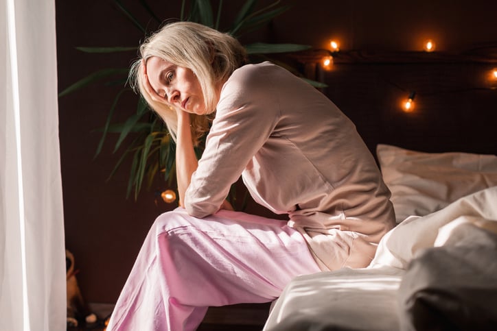 Vrouw zit op rand van het bed, is moe.