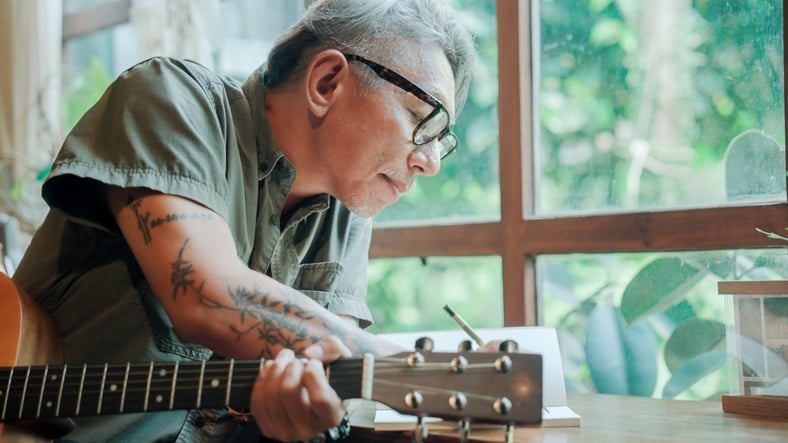 Man met gitaar in hand schrijft iets op