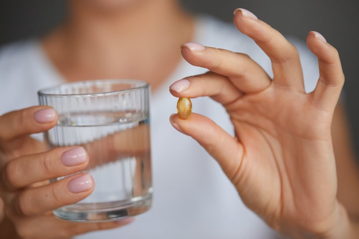 Een pil tussen twee vingers naast een glas water