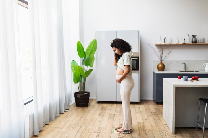 Zwangere vrouw weegt zichzelf op weegschaal in de keuken.