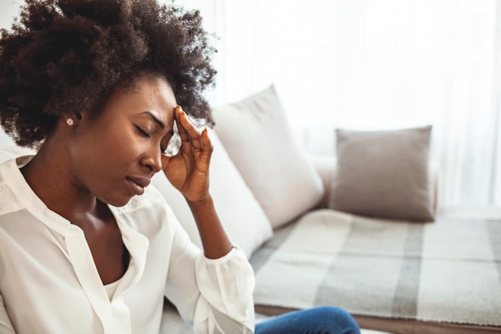 Vrouw met krullen zit op de bank met hoofdpijn