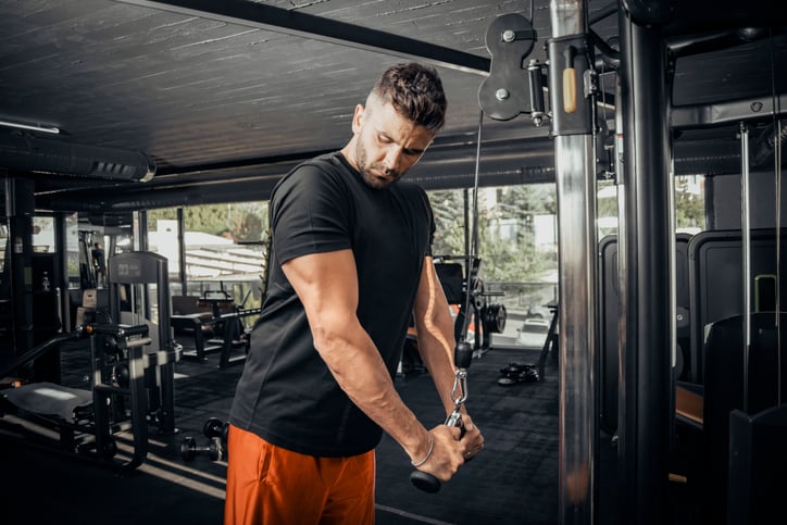 Man doet tricep pushdown in de gym