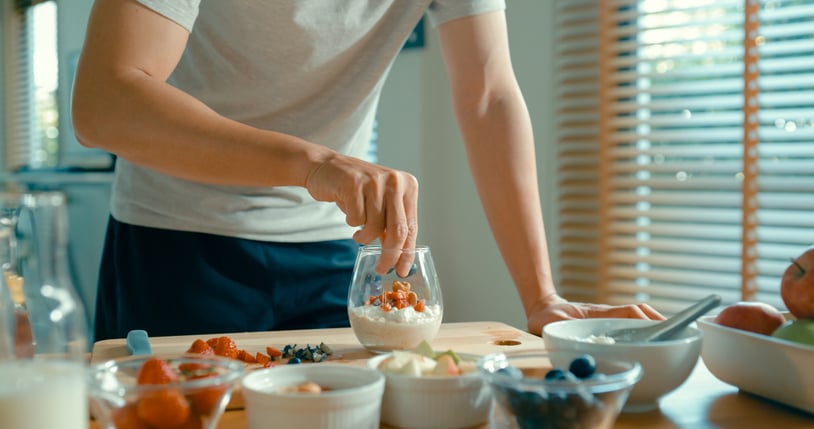 Man voegt verschillende fruitsoorten toe aan glas met yoghurt