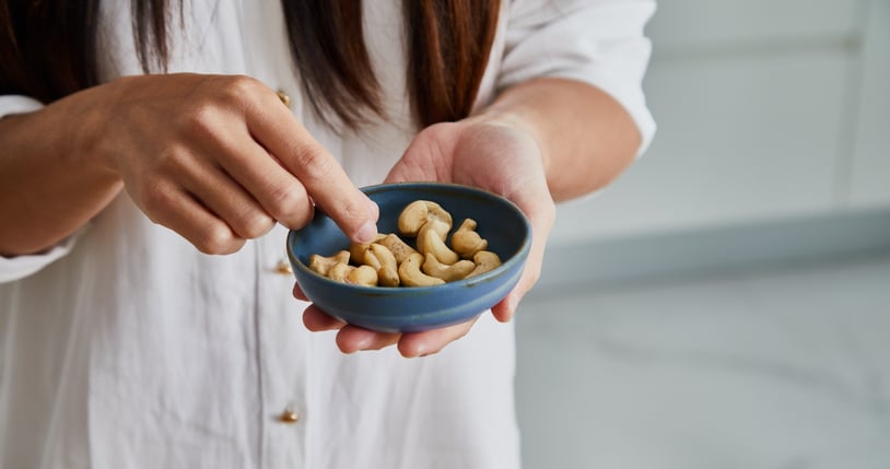vrouw heeft een bakje met cashewnoten vast