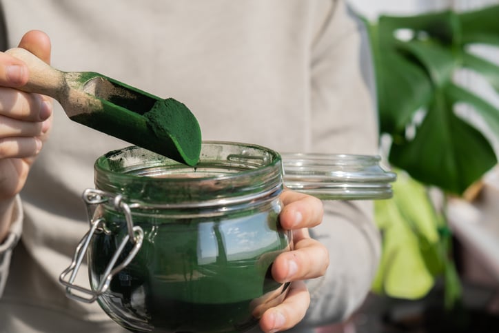 vrouw schept spirulina uit een glazen pot