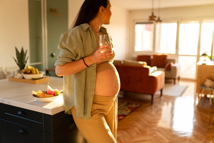 Zwangere houdt glas water vast en kijkt naar buiten