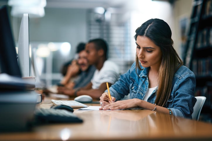 Vrouw zit gefocust achter een computer notities te maken